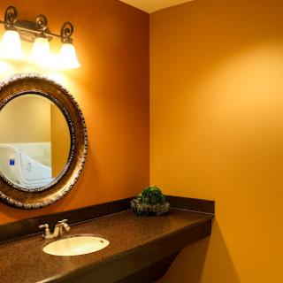 A stylish modern bathroom featuring an orange wall, a round mirror, and elegant lighting.