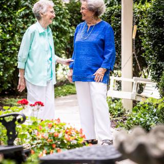 Two elderly women enjoying a conversation in a garden setting.