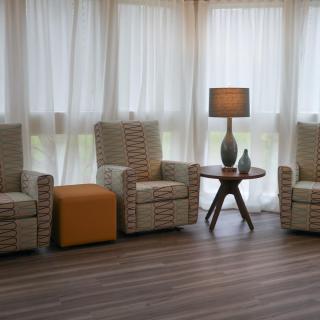 A cozy living room setting with three armchairs, a table with a lamp, and sheer curtains.