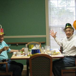Two men enjoying a festive meal with party hats in a cozy dining setting.