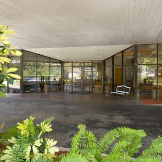 A modern glass entrance surrounded by lush greenery, showcasing minimalist architectural design.