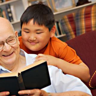 A grandfather and grandson enjoying a book together, sharing a joyful moment at home.