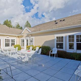 A sunny outdoor patio with white chairs and tables surrounded by a house.