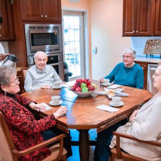 A group of seniors enjoying coffee and conversation around a kitchen table.
