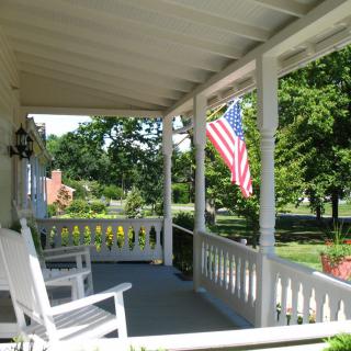 A charming front porch with rocking chairs and an American flag, overlooking a sunny landscape.