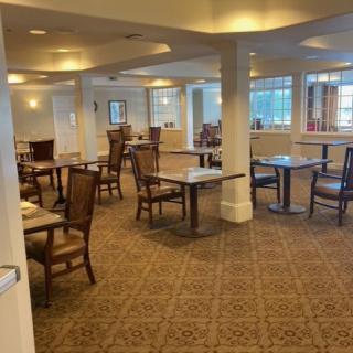 An empty dining room with neatly arranged tables and chairs on a carpeted floor.