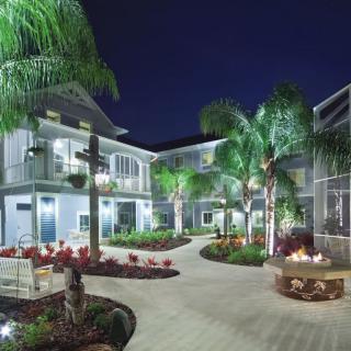 A beautifully lit hotel courtyard at night, featuring palm trees and a cozy fire pit.