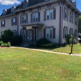 A large, two-story residential house with a well-maintained lawn on a sunny day.