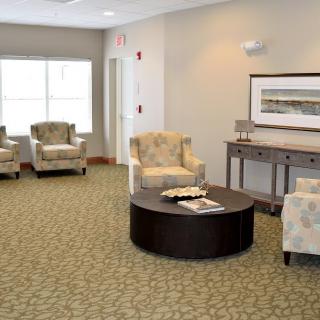 A well-furnished waiting room with comfortable chairs, a central table, and artwork on the wall.