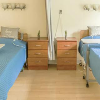 A hospital room with two beds, separated by a curtain, and equipped with bedside tables and medical equipment.