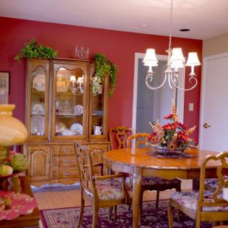 A cozy dining room with a wooden table, chairs, and a chandelier against red walls.