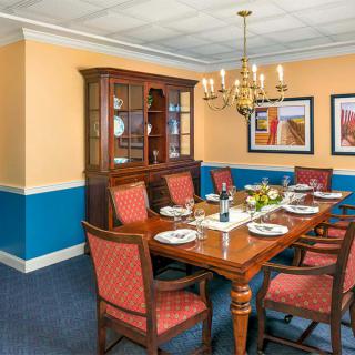 A well-decorated dining room featuring a wooden table set for a meal, surrounded by upholstered chairs and illuminated by a chandelier.