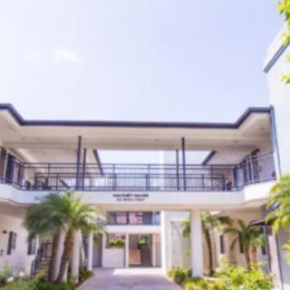 A modern building with a walkway and palm trees under a clear blue sky.