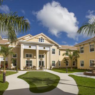 A residential building surrounded by palm trees under a sunny, cloudy sky.