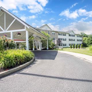 A welcoming entrance of a hotel with a driveway surrounded by lush landscaping under a bright blue sky.