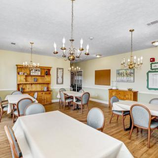 A cozy dining room with chandeliers, tables, and chairs on a wooden floor.