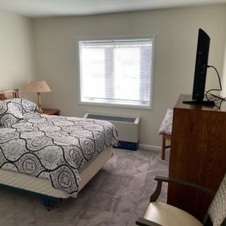 A cozy bedroom with a bed, dresser, TV, and a window letting in natural light.