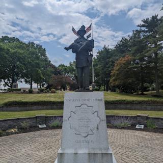 A statue standing prominently in a park, surrounded by greenery and under a partly cloudy sky.
