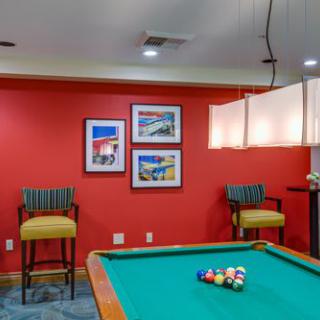 A cozy billiard room featuring a pool table, vibrant red walls, and stylish bar stools.