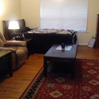 A cozy living room with an armchair, coffee table, bed, and lamp.