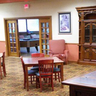 A cozy indoor room with tables, chairs, a cabinet, and a carpeted floor.