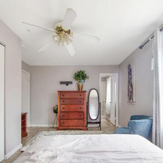 A cozy bedroom featuring a wooden dresser, an oval floor mirror, and a comfy blue chair.