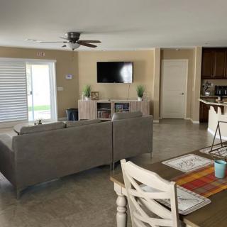 A modern open-plan living and dining area featuring a comfortable sofa, wall-mounted TV, and a neatly set dining table.