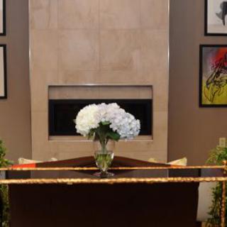 A modern living room setup featuring a vase of white flowers on a table in front of a fireplace, surrounded by framed artwork.