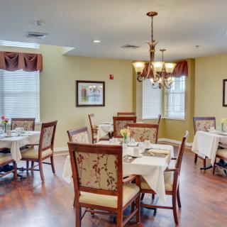 A cozy dining room with neatly arranged tables and chairs under a chandelier.