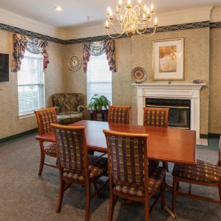 A formal dining room with a wooden table, chairs, and a chandelier above. A fireplace is present along with artwork on the wall.