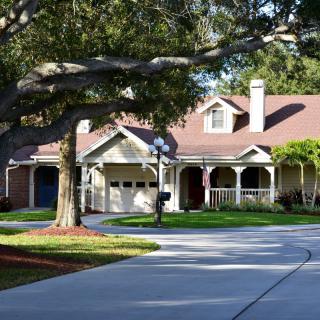 A suburban house with a spacious driveway surrounded by lush trees and landscaping.