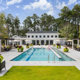 An outdoor swimming pool area with deck chairs and a modern building, surrounded by trees.