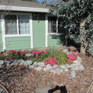 A charming garden with pink flowers and a rock border in front of a green house.