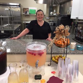 A person standing behind a kitchen counter with beverages and snacks displayed.