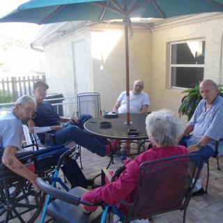 A group of people sitting and socializing on a patio under an umbrella.