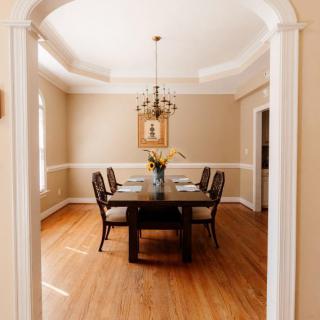 A well-lit dining room with a wooden table and chairs, featuring a chandelier and classic decor.
