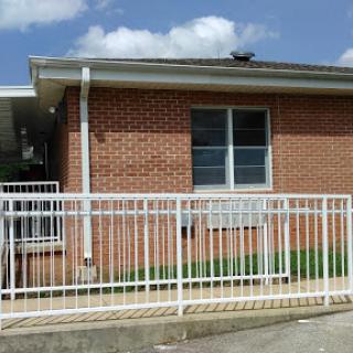 A residential brick building with a white fence and air conditioner visible on the wall.