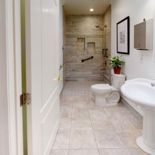 A modern bathroom with a tiled floor, featuring a toilet, sink, and spacious shower area.