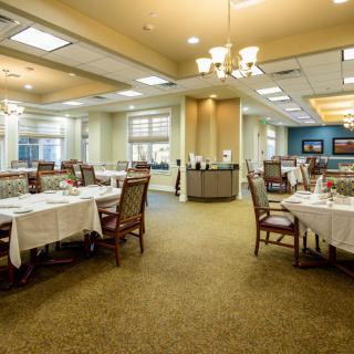 An elegant dining room with neatly arranged tables and chairs, illuminated by chandeliers.