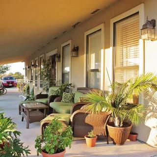 A cozy porch with outdoor furniture and potted plants bathed in sunlight.