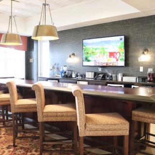 A cozy bar area featuring a long counter with high chairs, pendant lighting, and a large TV on the wall.