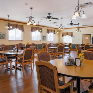 A spacious dining room with neatly arranged tables and chairs, featuring elegant lighting fixtures and large windows.