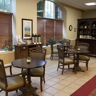 Cozy cafe interior with tables, chairs, and a coffee station near large windows.