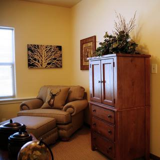 A cozy living room corner featuring a comfortable chair, wooden cabinet, and decorative artwork.