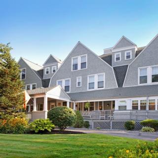 A charming multi-gabled house with a manicured lawn and trees under a clear blue sky.
