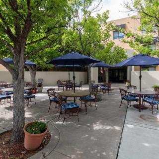 A peaceful patio area with outdoor seating, featuring tables and chairs under blue umbrellas surrounded by greenery.