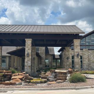 A modern building with stone architecture and well-maintained landscaping under a cloudy sky.