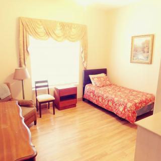 A cozy bedroom with a single bed, furnished with a chair, dresser, and a window adorned with curtains.