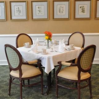 A neatly set dining table with four chairs, featuring a white tablecloth and decorative artwork on the walls.