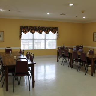 An empty dining room with wooden tables and chairs, featuring a large window with curtains.